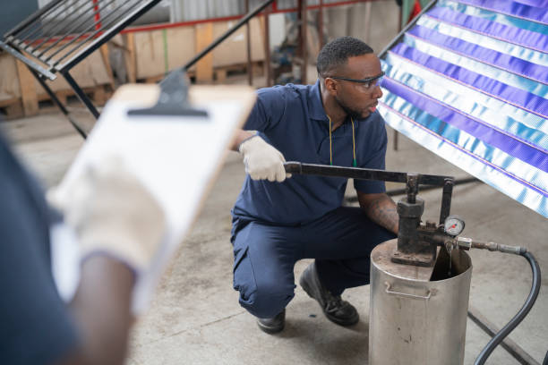 An african-american supervisor is overseeing a worker pumping water into a panel for testing at a solar panel factory